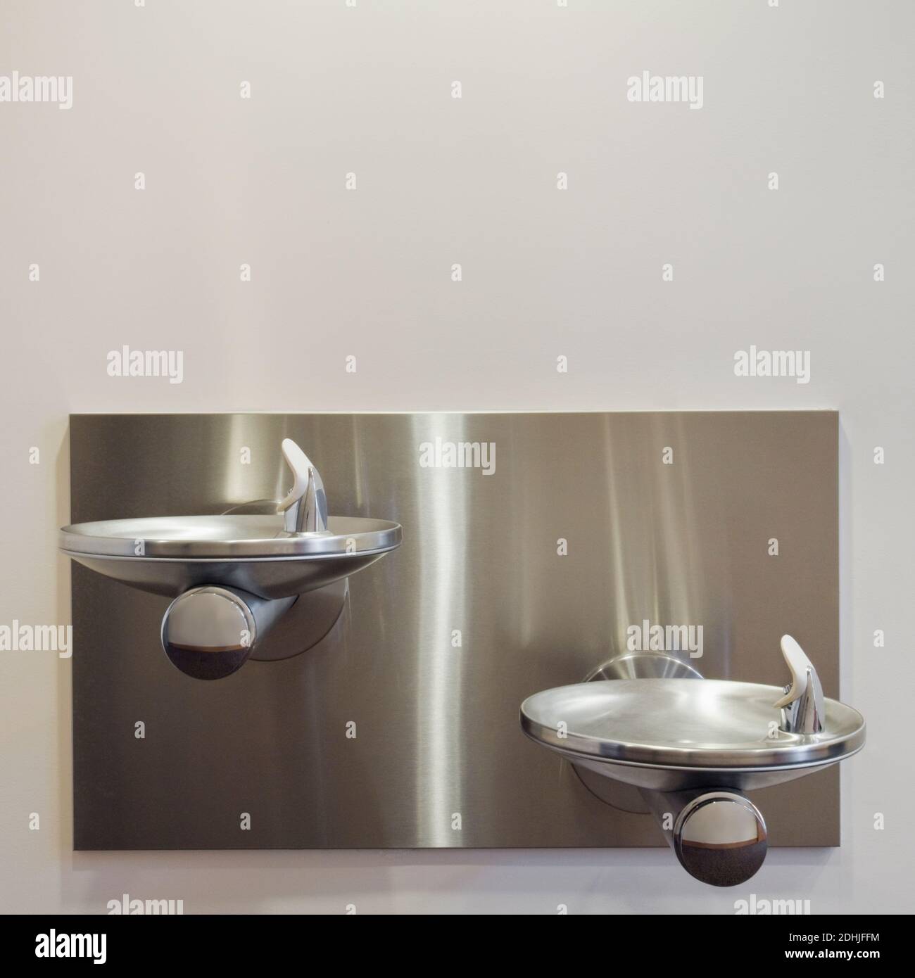 Two metal drinking fountains mounted on wall at different heights Stock