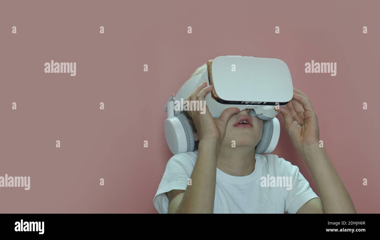 A little boy is watching a video in virtual glasses on a pink background. Stock Photo