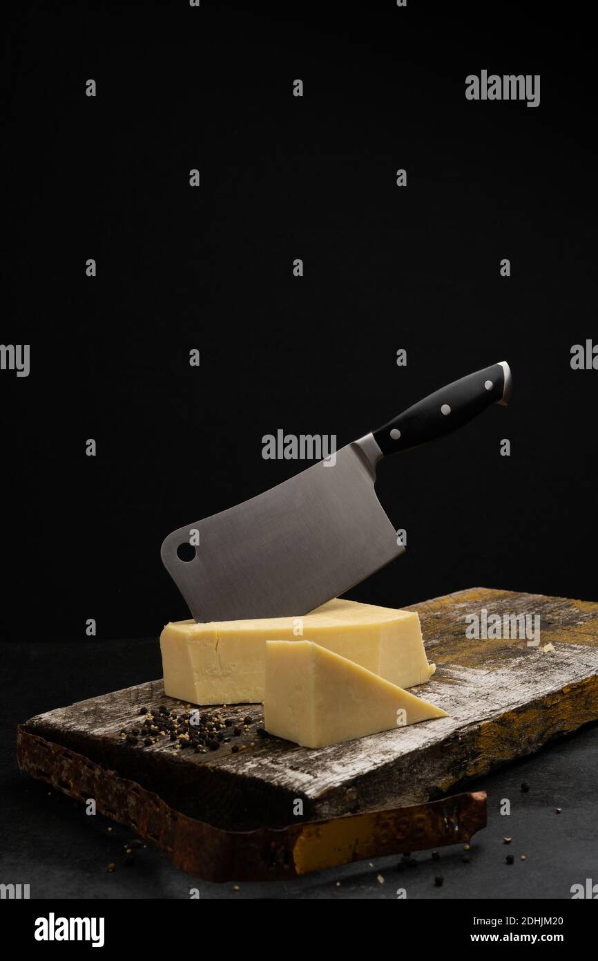 Welsh cheddar with kitchen cleaver embedded, on a wooden scaffold board on top of Welsh slate base Stock Photo