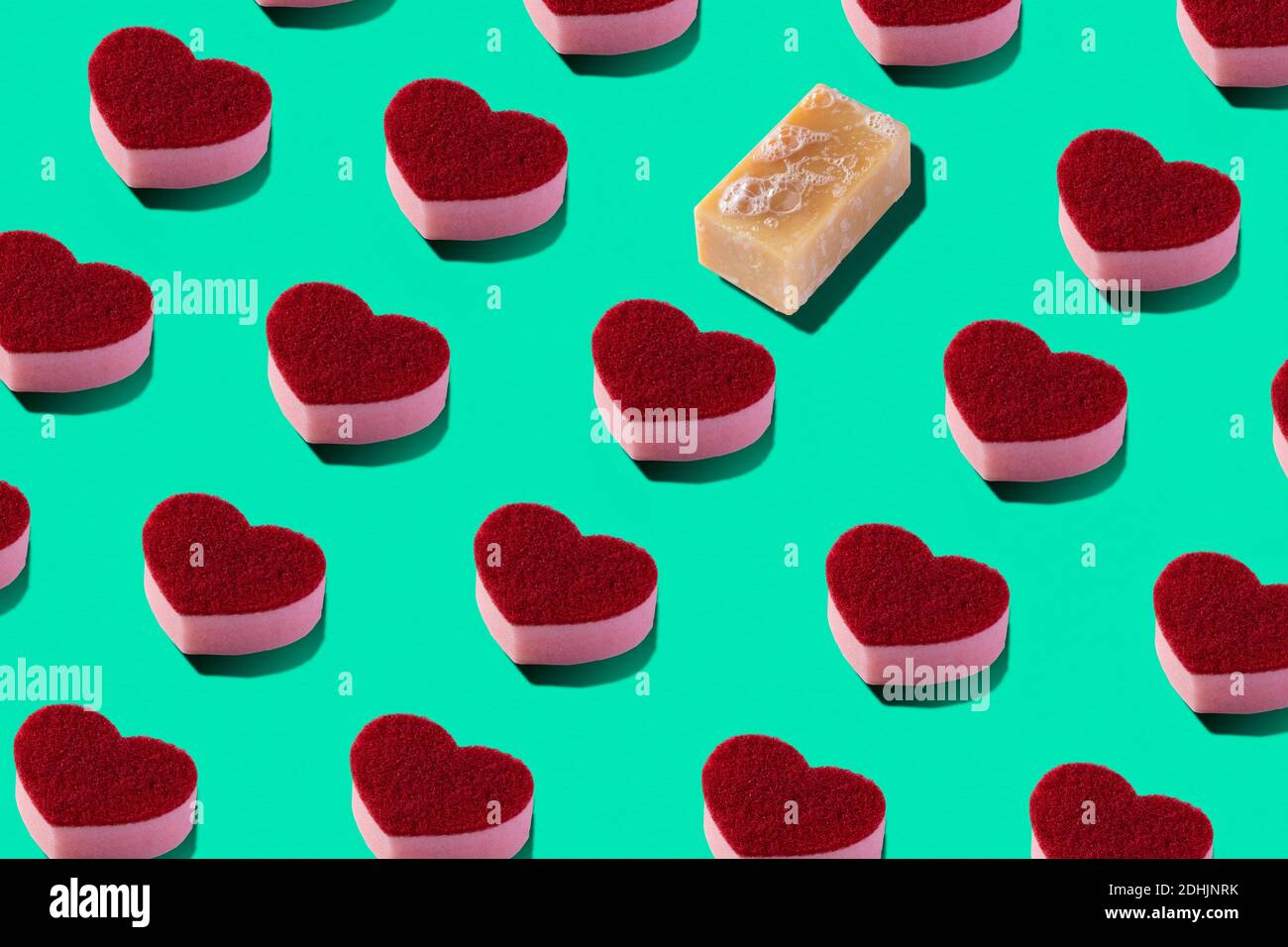 From above full frame composition of red heart shaped soap arranged in order on light green background with one different Stock Photo
