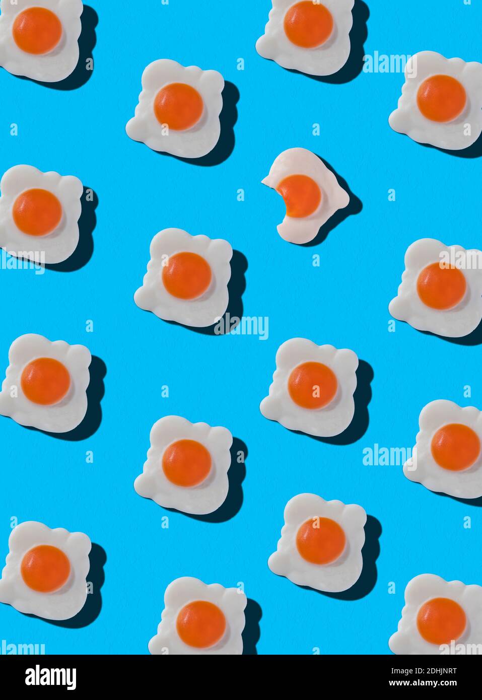 Top view of pattern of whole sweet candies in shape of fried eggs with one bitten arranged on blue background Stock Photo