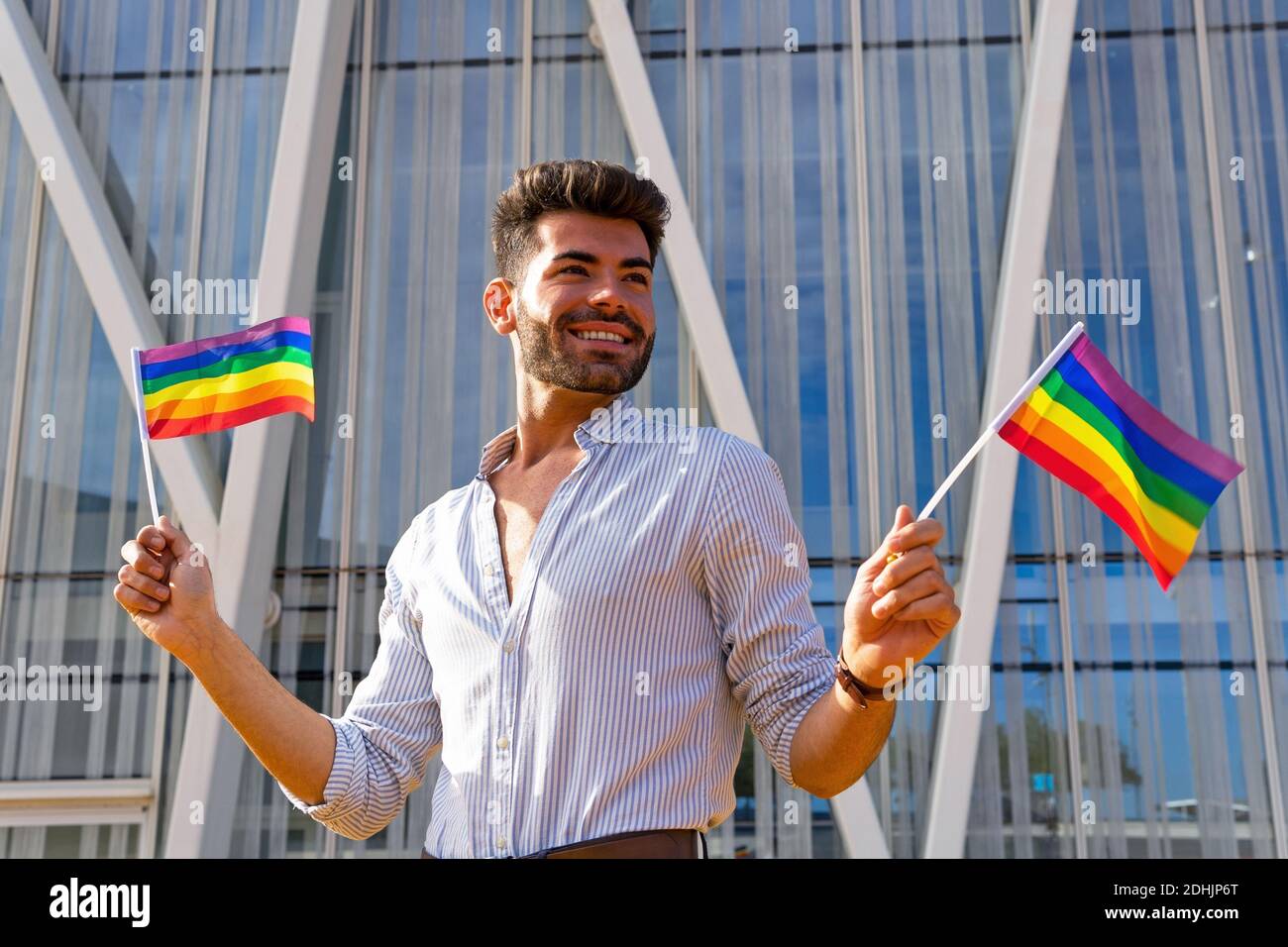 Low angle of delighted homosexual male standing on street with paper ...