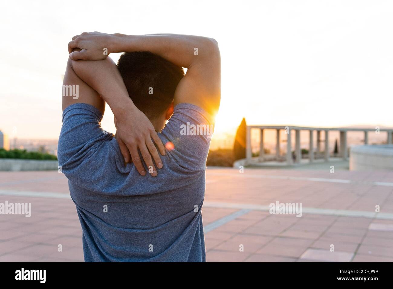 Back view of unrecognizable flexible male stretching arms while practicing yoga and enjoying sundown in summer Stock Photo