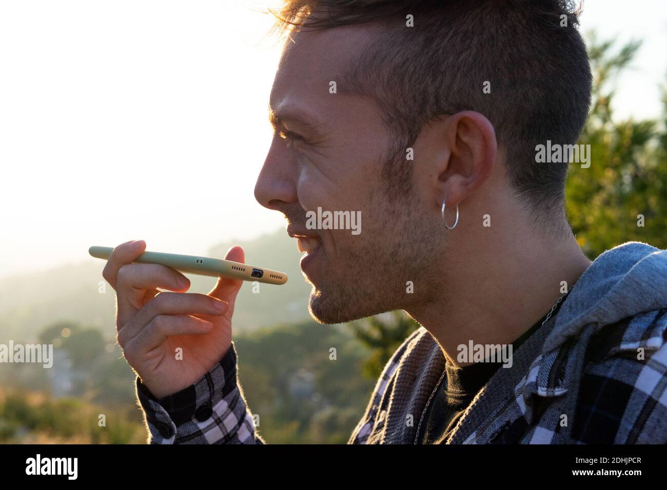 Young cheerful tourist in face mask and eyeglasses standing near river behind mountains while looking away Stock Photo