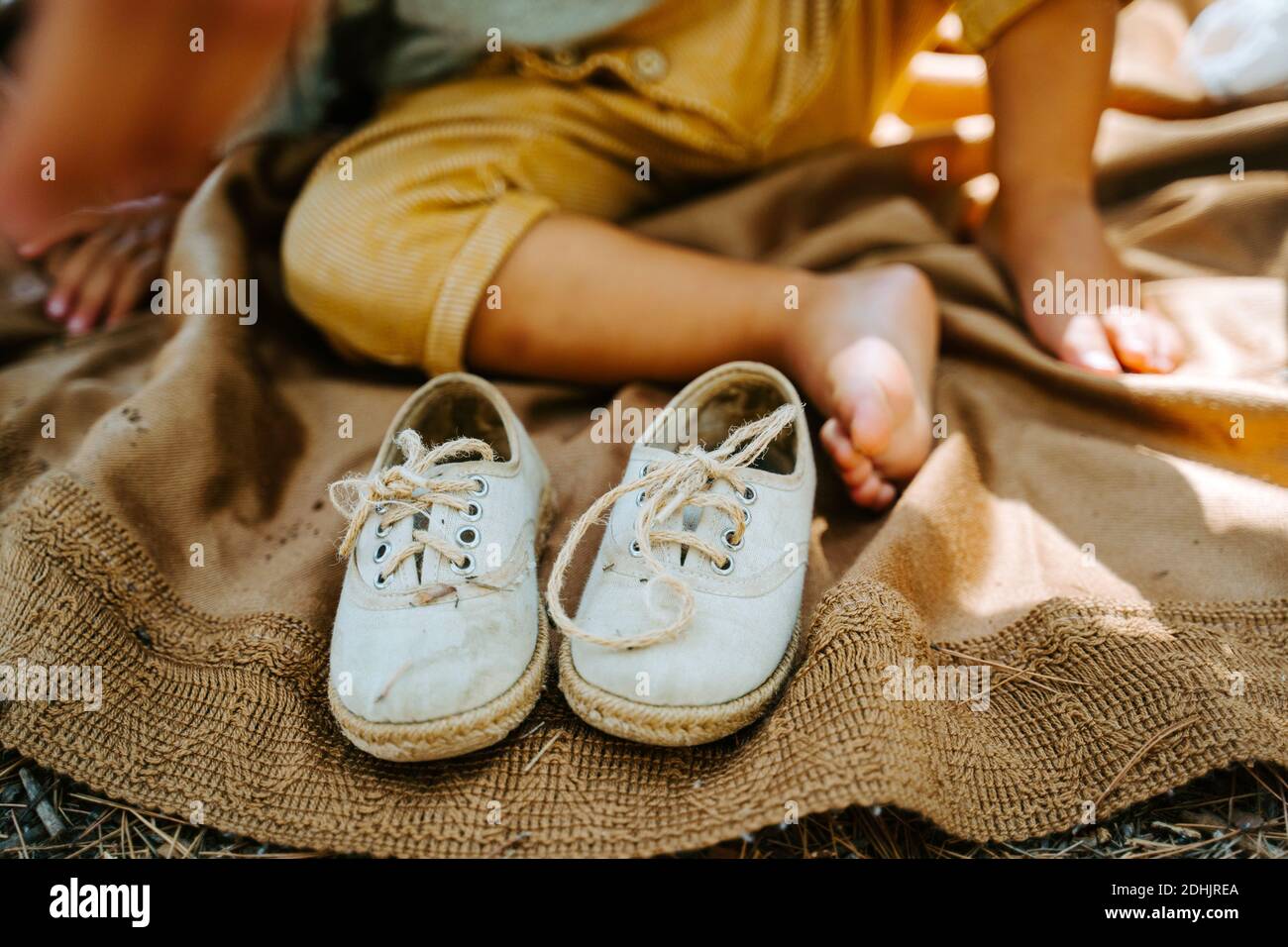 Fabric shoes placed on blanket on background of crop anonymous kid sitting barefoot in nature Stock Photo