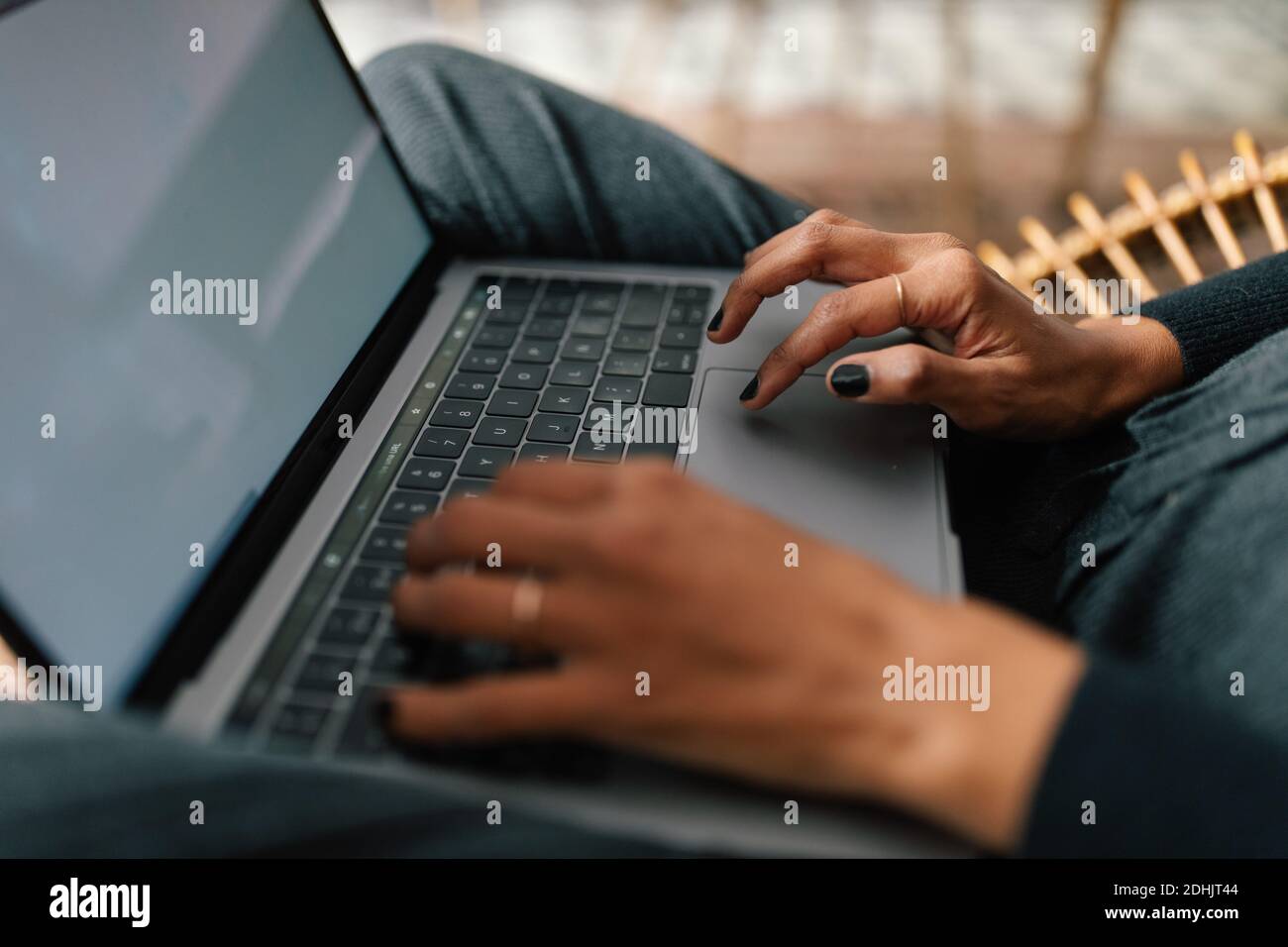 Side view of crop faceless ethnic female entrepreneur sitting in chair at home and working on online project while using netbook Stock Photo