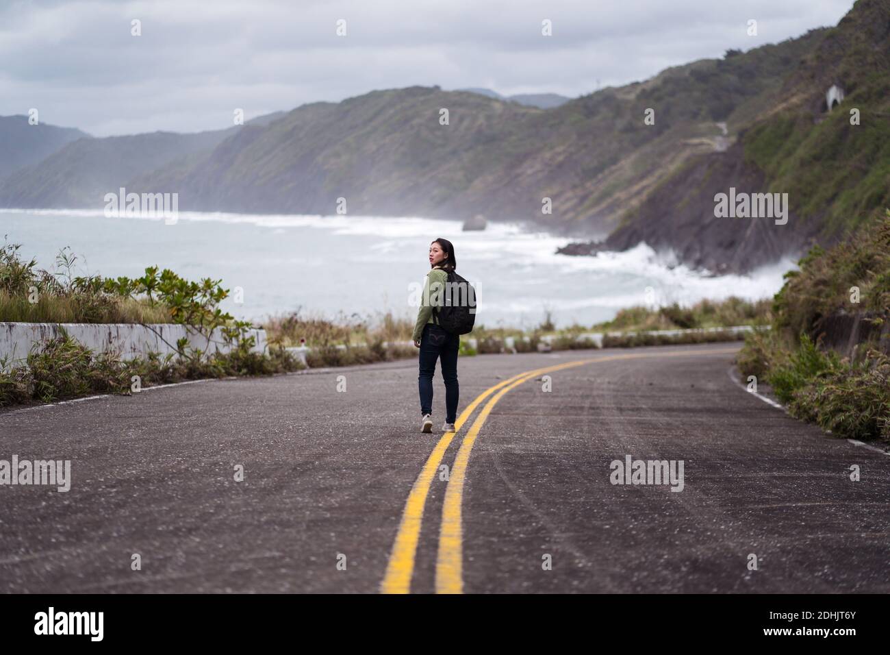 Back view of active female hiker with backpack walking on asphalt road ...