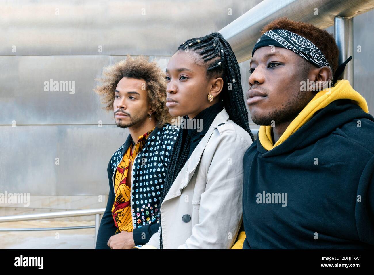Serious unemotional young African American friends in casual informal clothes standing on stairway looking away while spending time together in city Stock Photo
