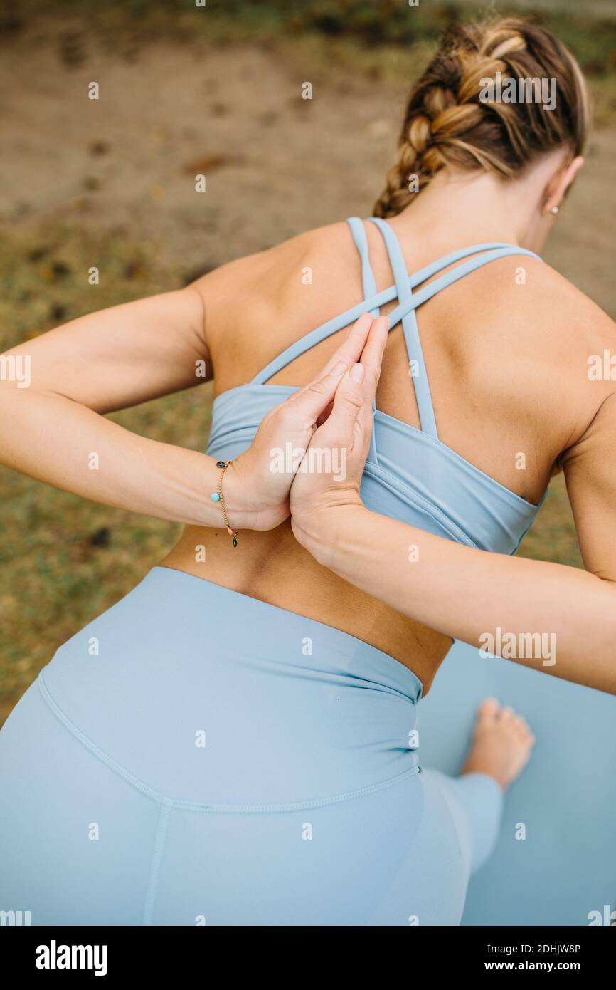 Back view of slim female in sportswear doing Half Pyramid Pose with Prayer Hands Behind Back while practicing yoga in nature Stock Photo