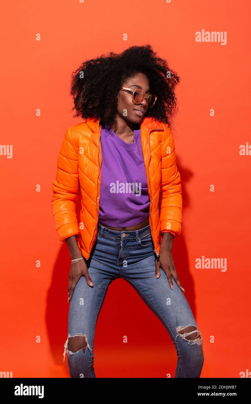 Young black female in purple shirt with denim and orange jacket standing on  red background looking down Stock Photo - Alamy