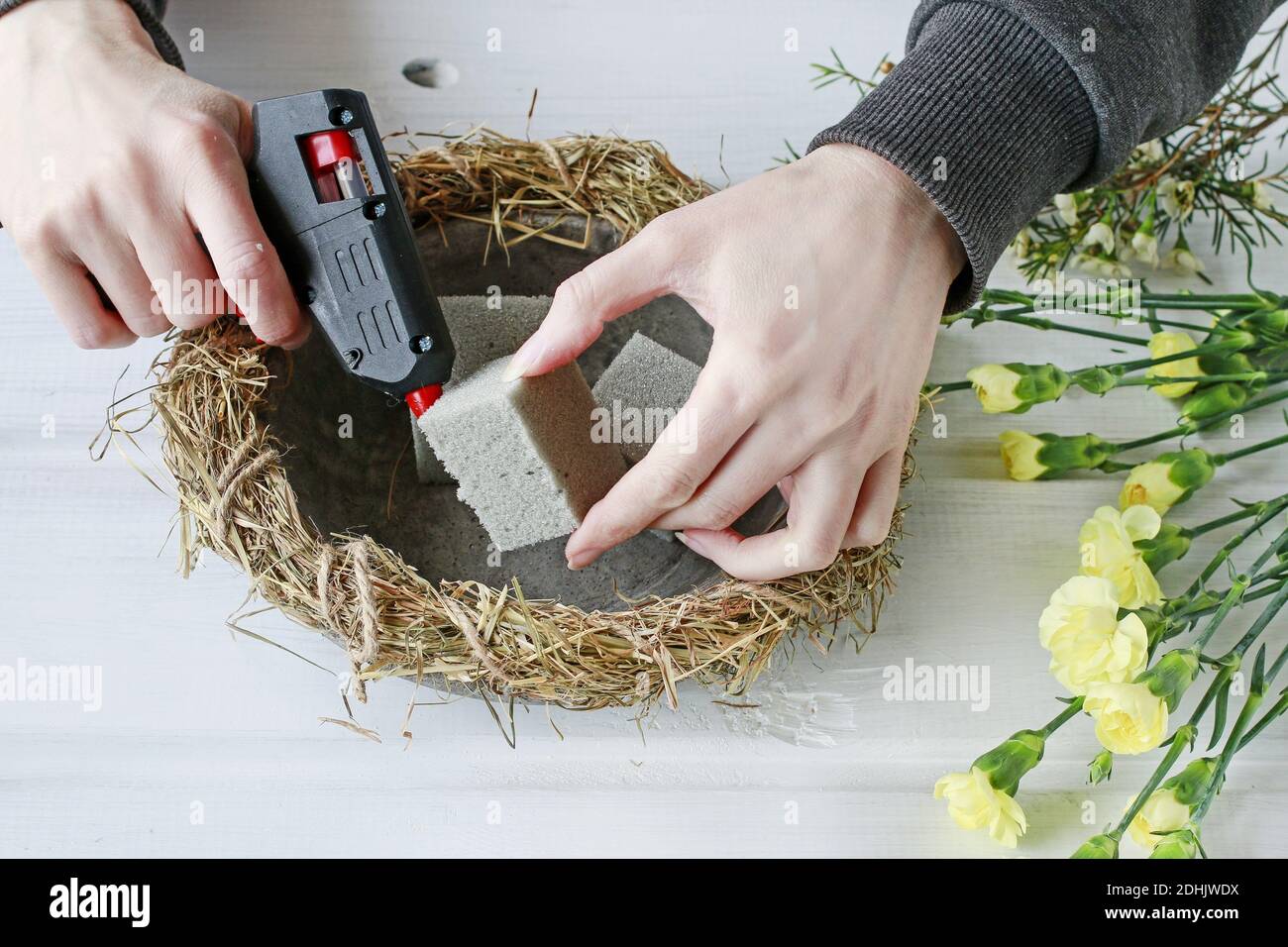 Florist at work: How to make Easter table centerpiece with carnations, wax flower, eggs and moss. Step by step, tutorial. Stock Photo