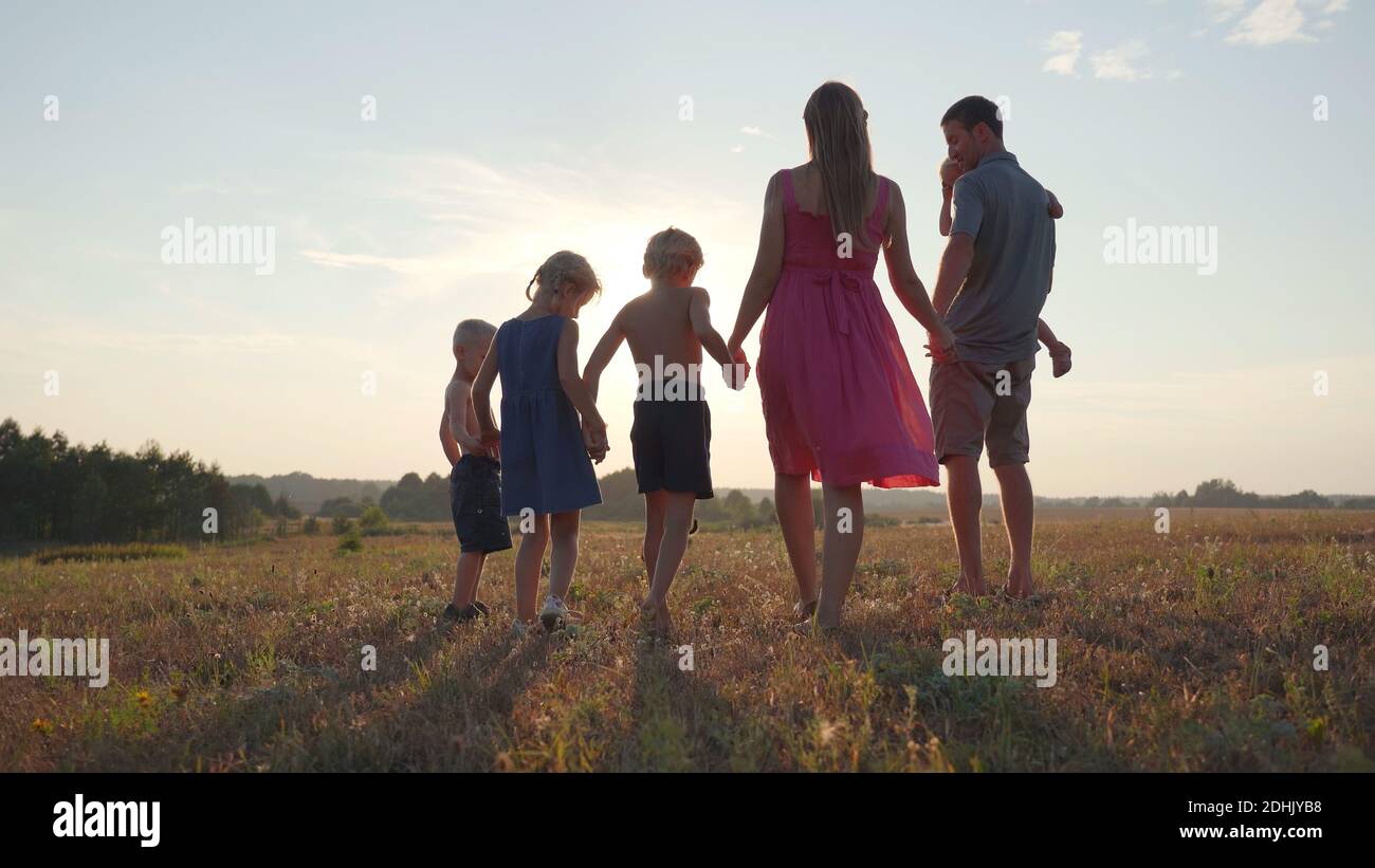 A friendly large family walks across the field at sunset with dog Stock ...