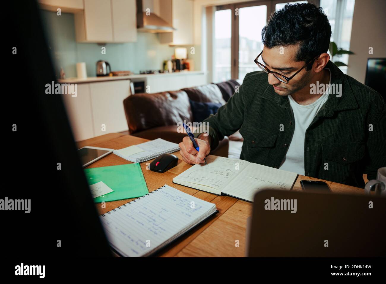 mixed race businessman writing in note pad working from desktop computer  Stock Photo