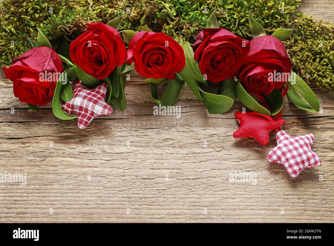 Red roses, mistletoe, fabric stars and moss on wooden background, copy space. Stock Photo