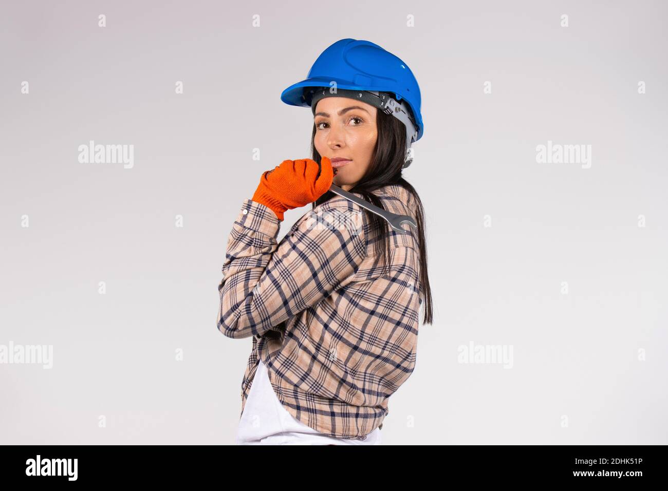 A woman mechanic in a hard hat holds a wrench on a white background looking at the camera. Side space for advertisment Stock Photo