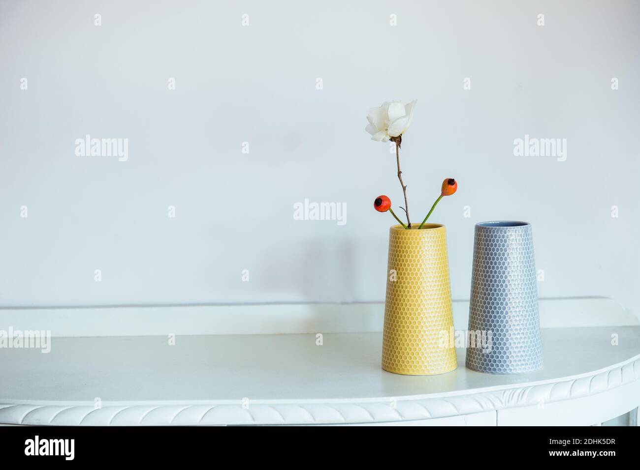 Two stylish grey and yellow vases wth flowers on pastel neutral