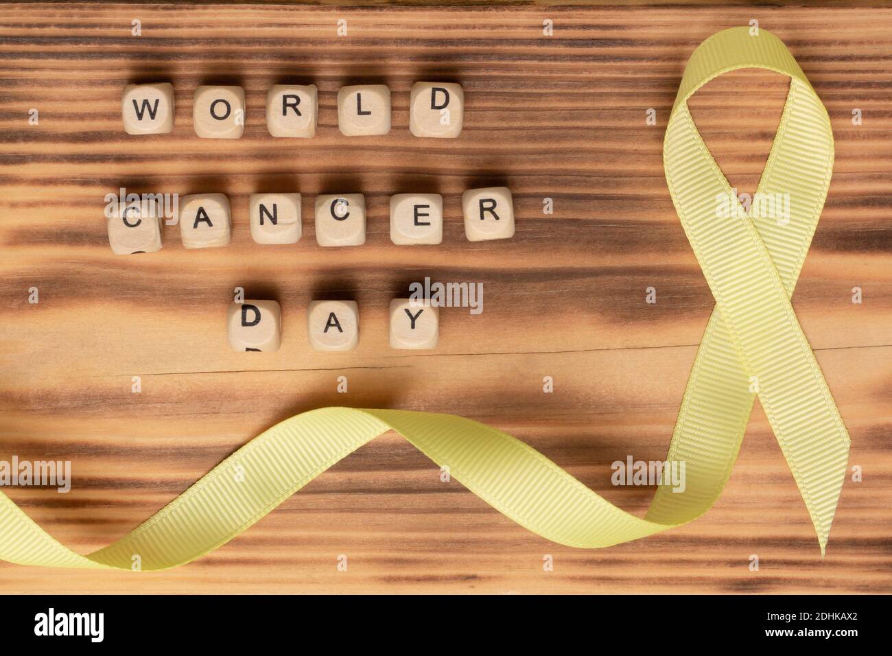 Wooden cubes with World Cancer Day text and yellow ribbon, on a wooden surface. Flat lay Stock Photo
