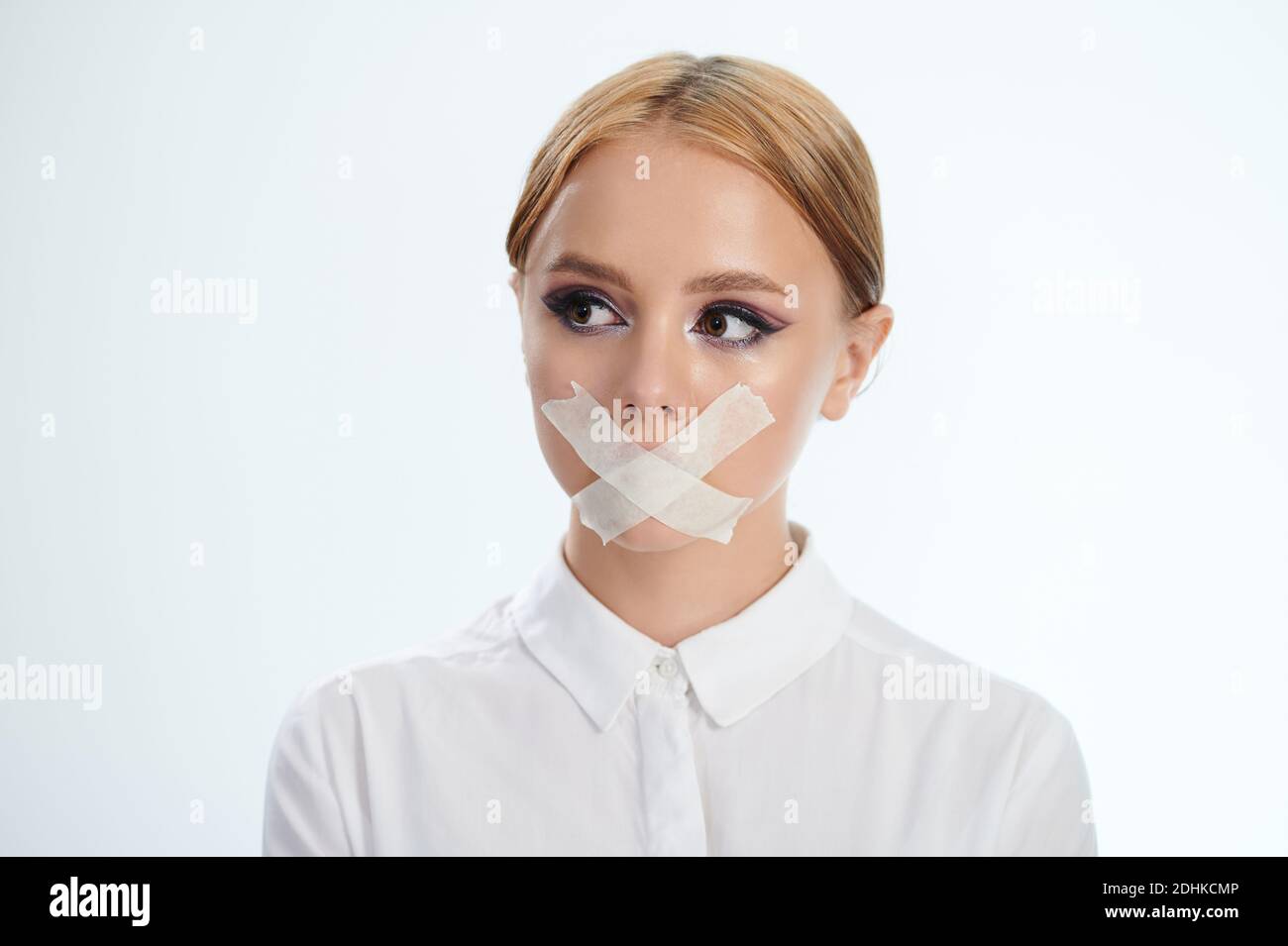 Portrait of girl with tape on mouth isolated on studio background Stock Photo