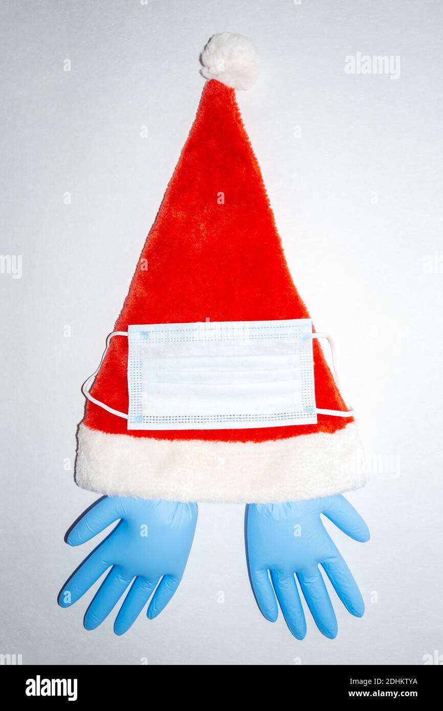 Red and white plush Christmas Santa hat with surgical mask and one pair of inflated blue medical vinyl gloves. Vertical top view Stock Photo