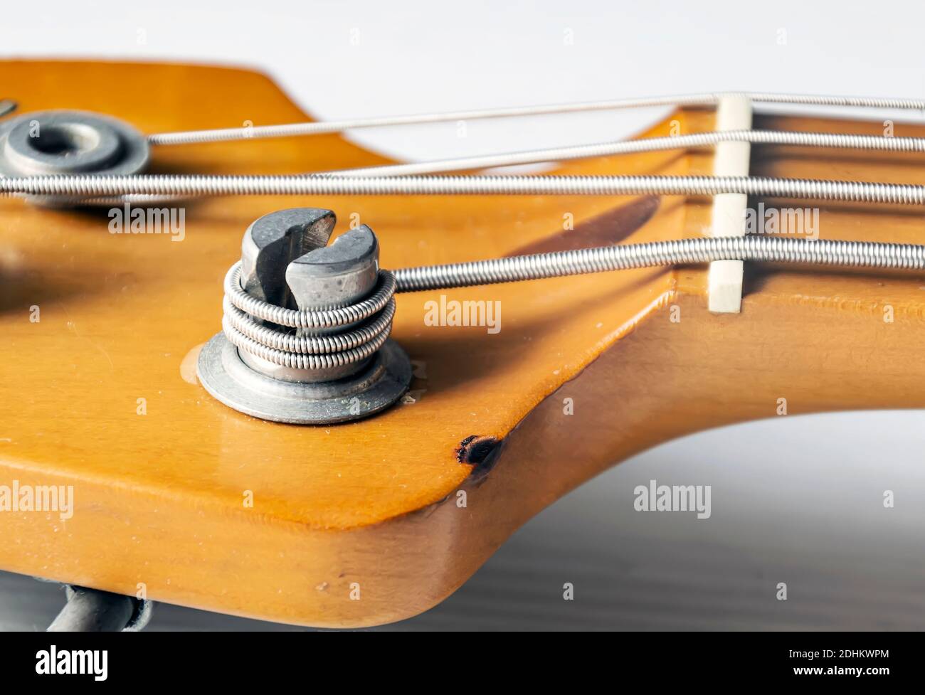 Detail of a tuning post on the wooden headstock of an electric bass guitar. Musical instruments and mechanics for string tuning. Stock Photo