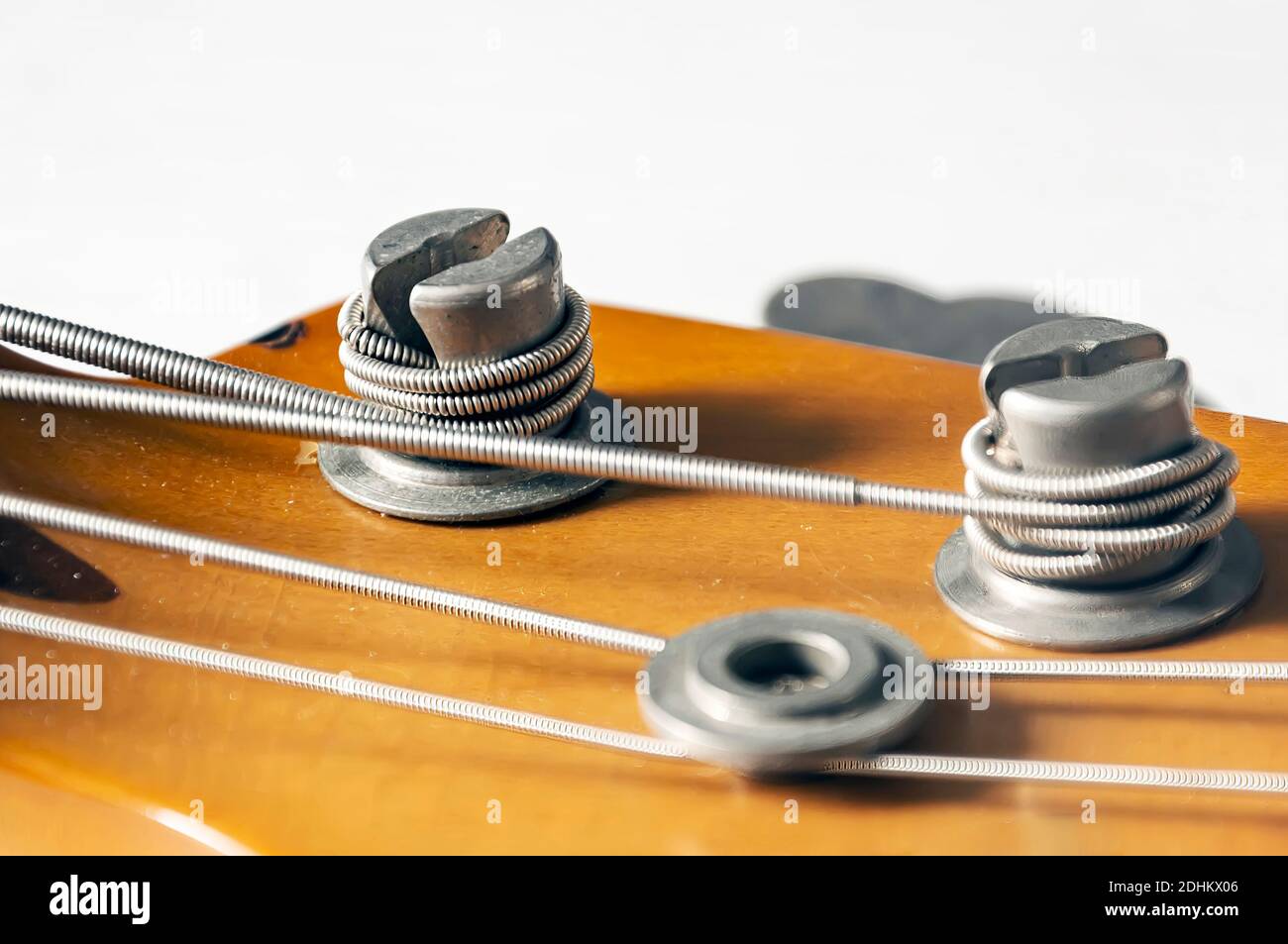 Detail of a tuning post on the wooden headstock of an electric bass guitar. Musical instruments and mechanics for string tuning. Stock Photo