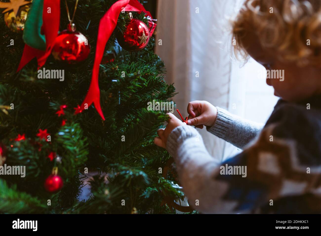 cute little child boy decorating christmas tree indoors during holidays season. family christmas time at home. in winter with warm natural soft light Stock Photo