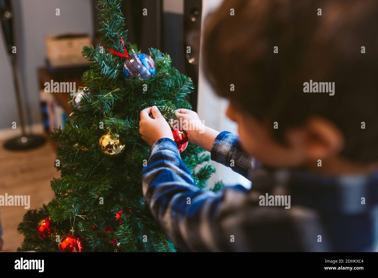 family christmas time at home. cute little child boy decorating christmas tree indoors during holidays season. in winter with warm natural soft light Stock Photo