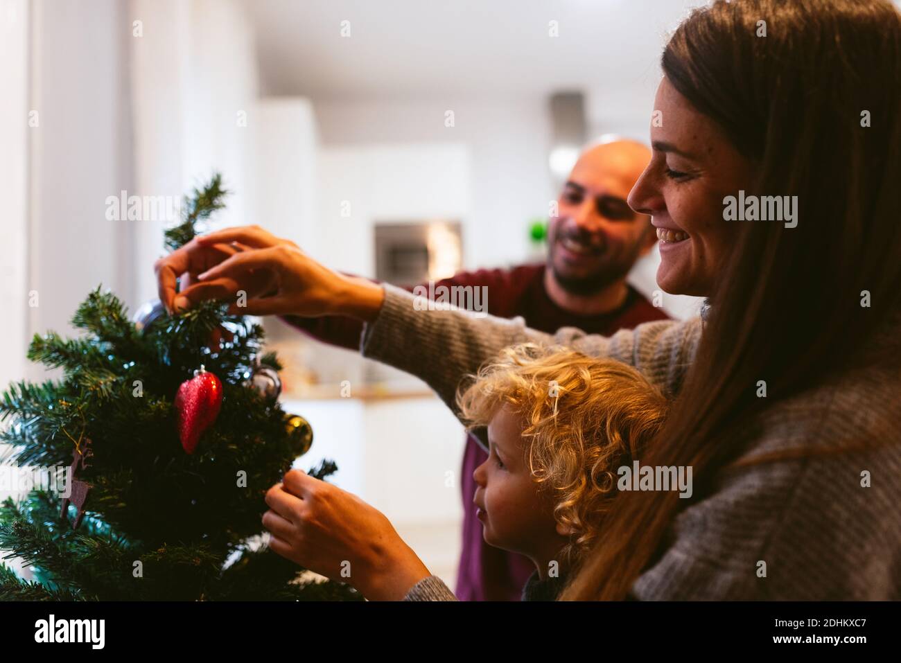 happy family christmas time at home. smiling mother and father with cute children decorating christmas tree together. candid family unit and christmas Stock Photo