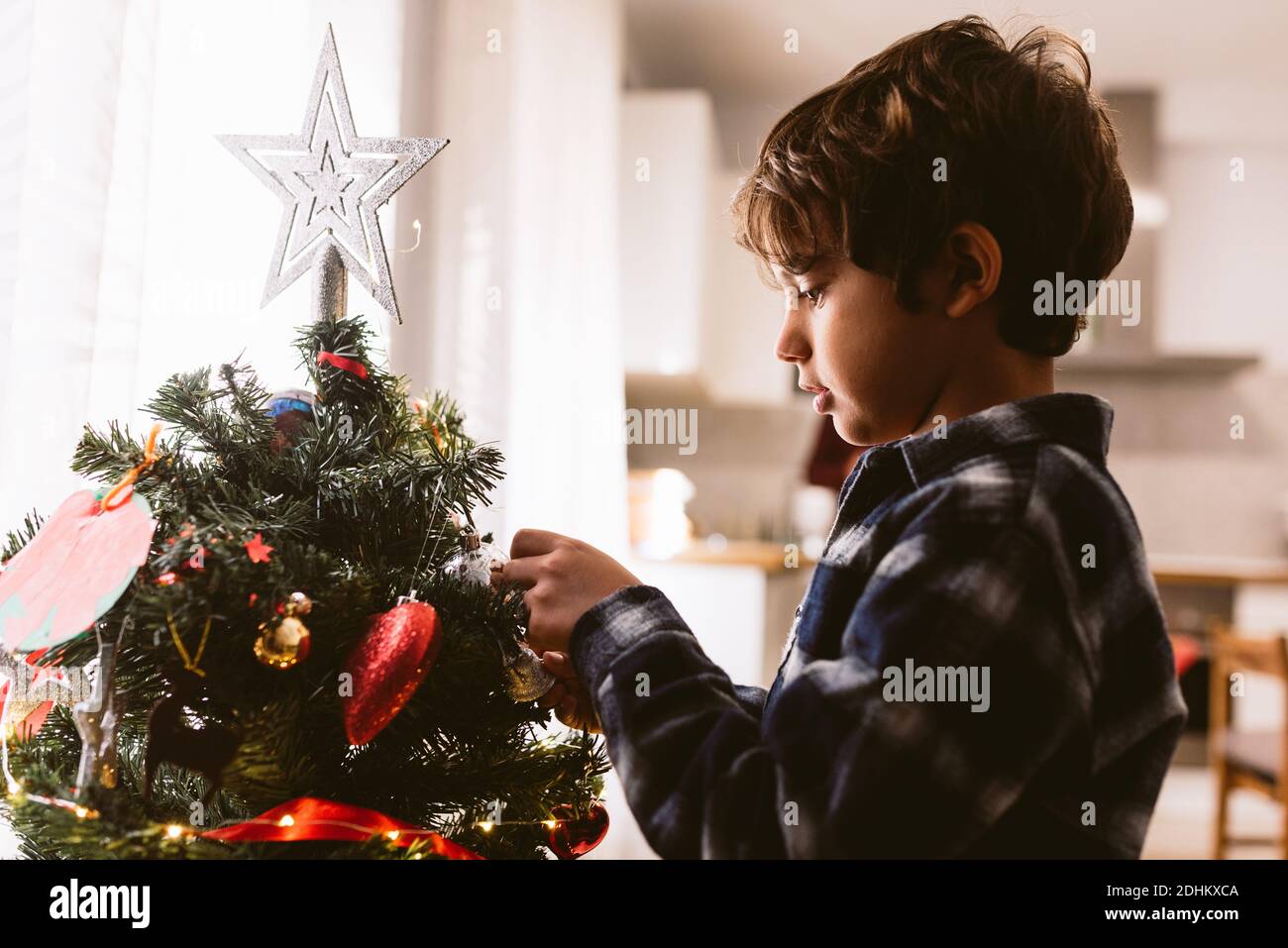closeup of cute little child boy decorating christmas tree indoors during holidays season. family christmas time at home. in winter with warm natural Stock Photo