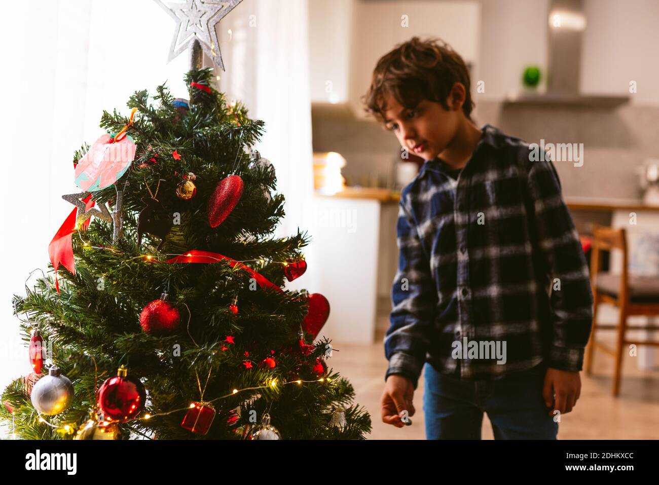 cute little boy decorating christmas tree indoors during holidays season. family christmas time at home. in winter with warm natural soft light from w Stock Photo