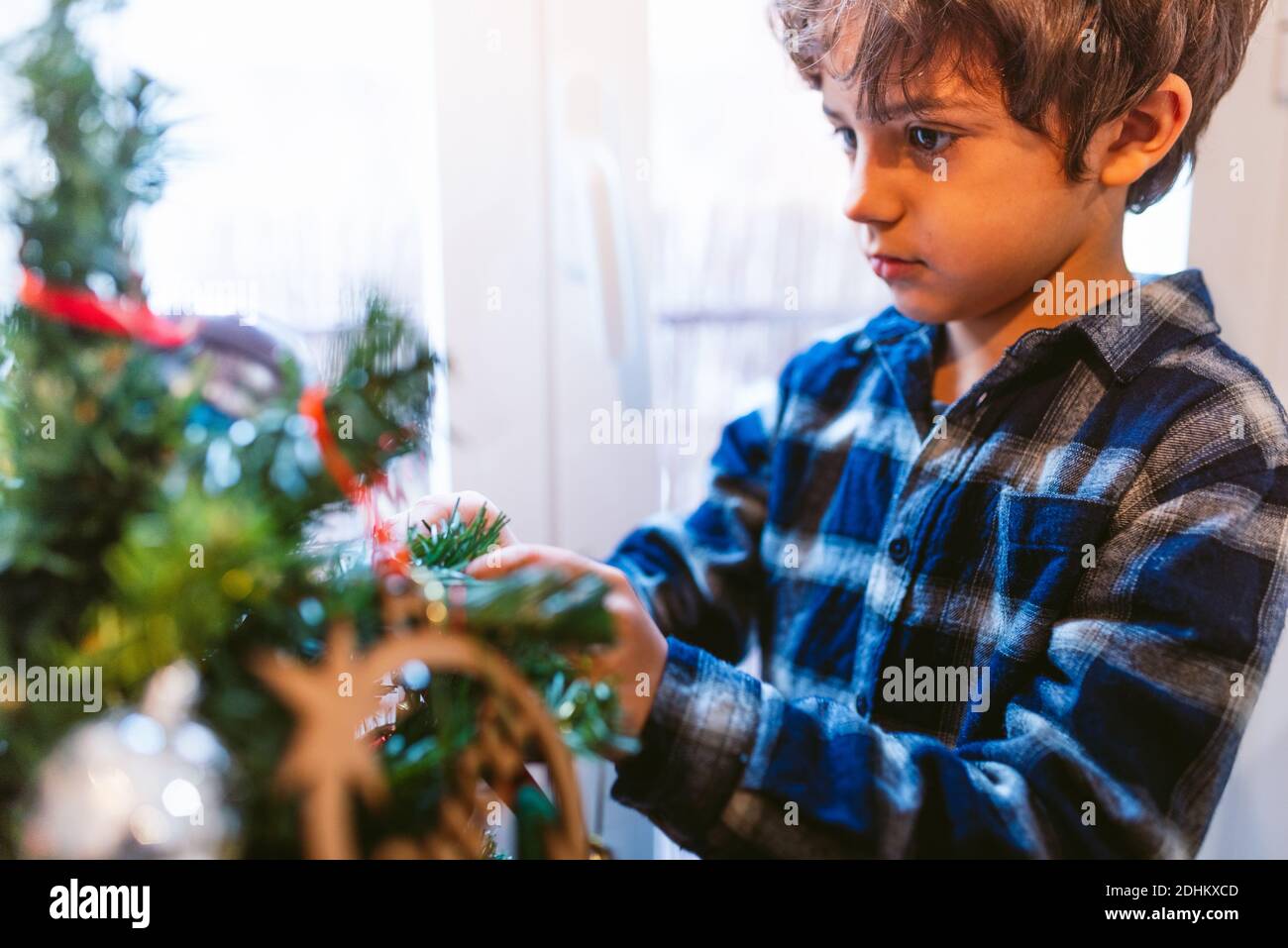 cute little child decorating christmas tree at home during holidays season. childhood christmas time at home. in winter with warm natural soft light Stock Photo