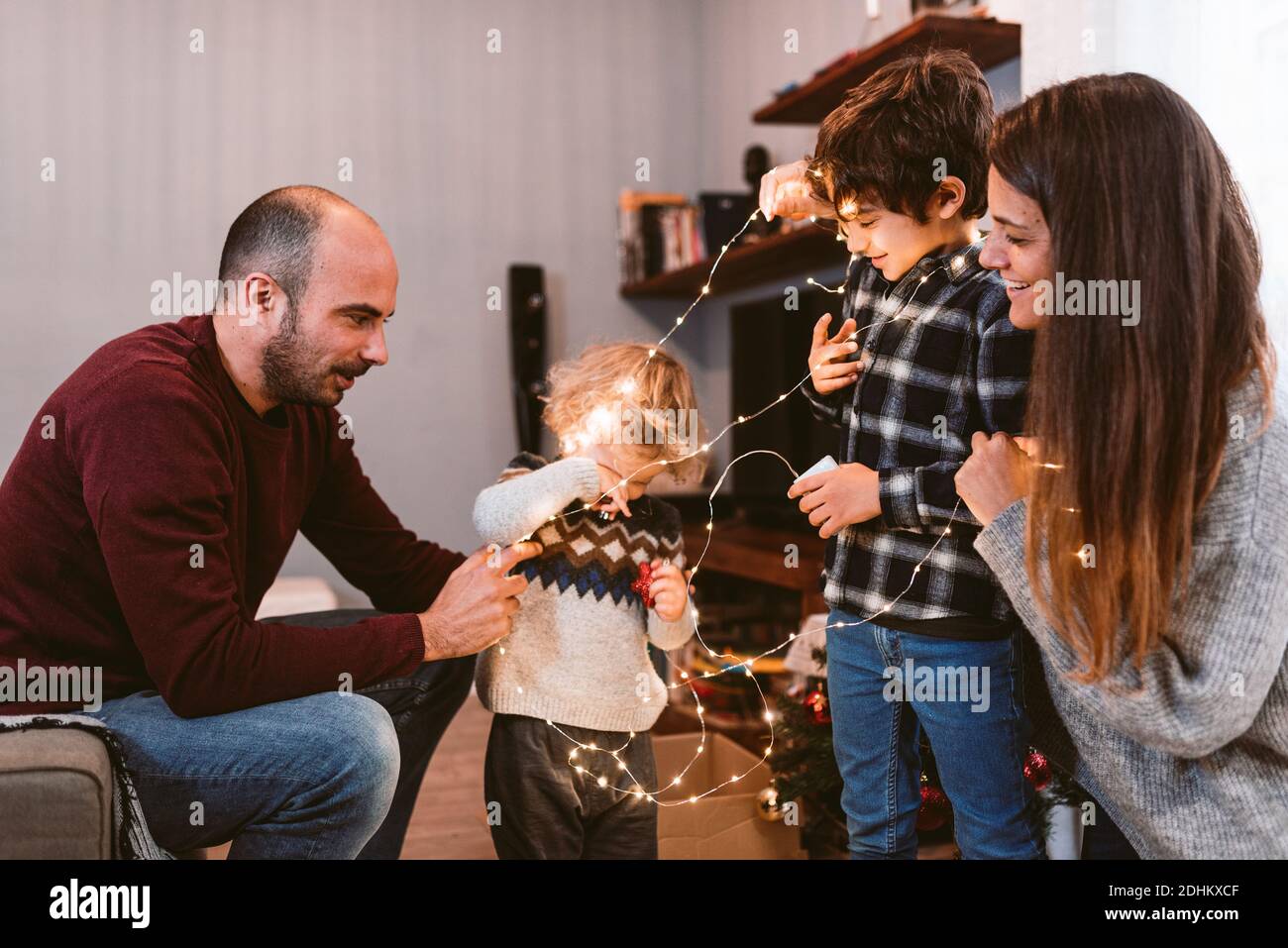 happy family christmas time at home. smiling mother and father with cute children decorating christmas lights together. family unit and christmas spir Stock Photo