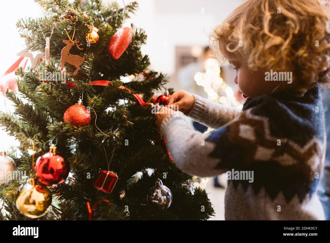 portrait of cute little blond child boy decorating christmas tree indoors during holidays season with christmas lights. family christmas time at home. Stock Photo