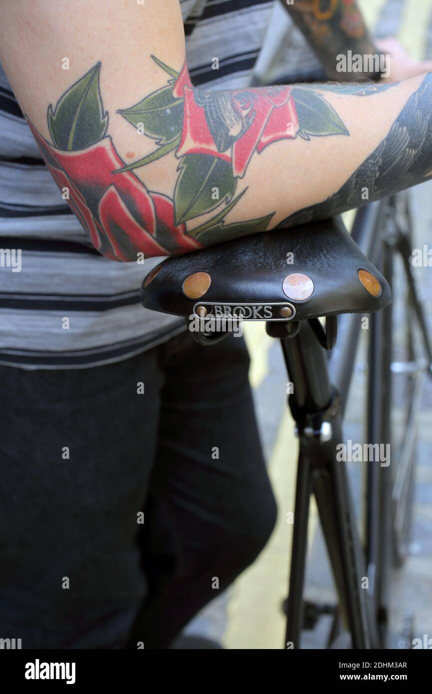 Close up of man with tattoo holding a bicycle with Brooks saddle . Stock Photo