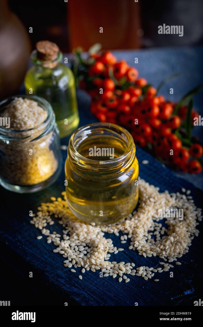Sesame oil in glass and seeds. Fresh sesame oil in a glass bottle and seeds on blue background. Stock Photo