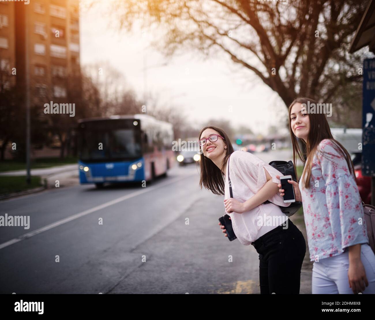 Two adorable cute high school girls waiting for a bus with backpacks on