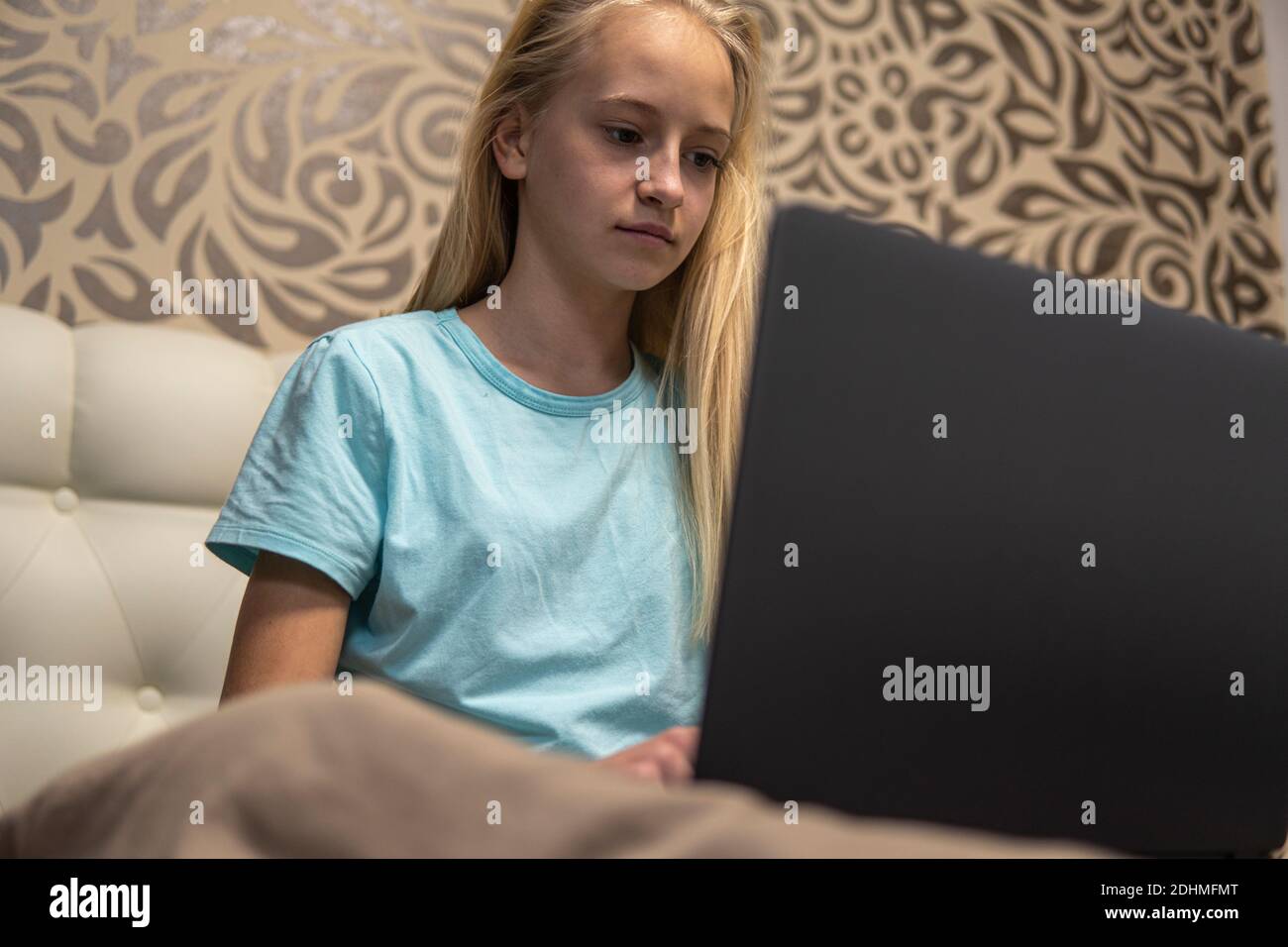 Teenage girl with blond hair working on laptop in bed. high quality Stock Photo