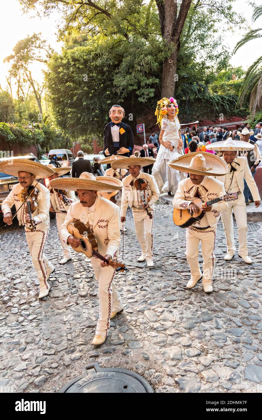 A traditional Mexican mariachi band plays as giant puppets called mojigangas dance during a wedding celebration parading through the streets San Miguel de Allende, Guanajuato, Mexico. Stock Photo
