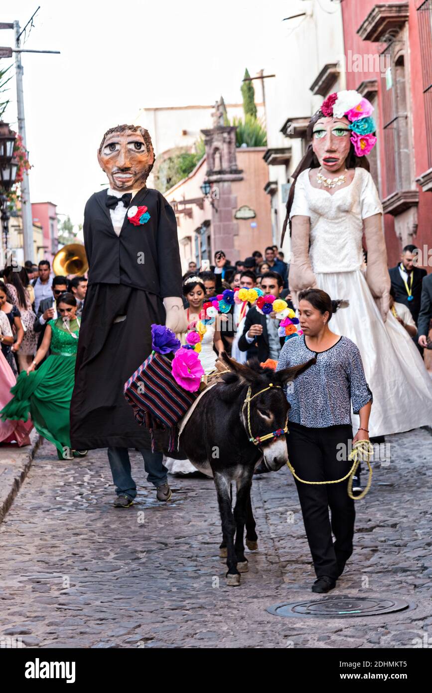 A decorated donkey leads the way as giant puppets called mojigangas dance during a wedding celebration parading through the streets San Miguel de Allende, Guanajuato, Mexico. Stock Photo