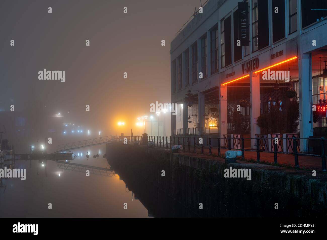 Harbourside warehouses converted into bars are shrouded in fog on an autumn night on Bristol's Floating Harbour. Stock Photo
