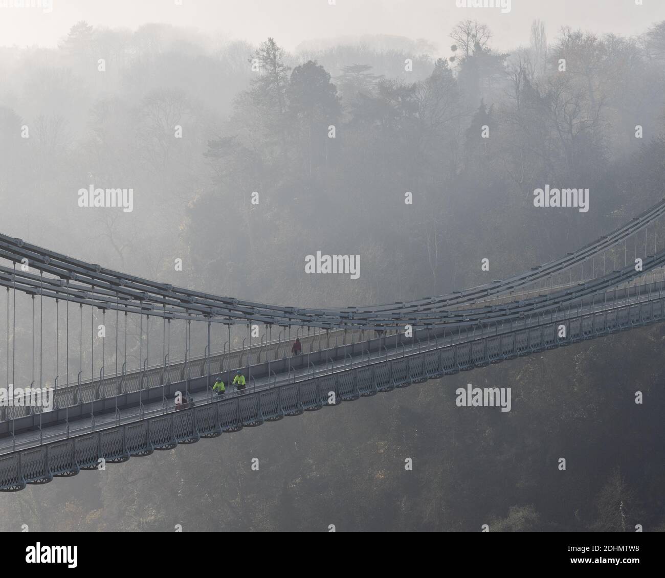 Cyclists ride across the landmark Clifton Suspension Bridge on a misty morning in Bristol. Stock Photo