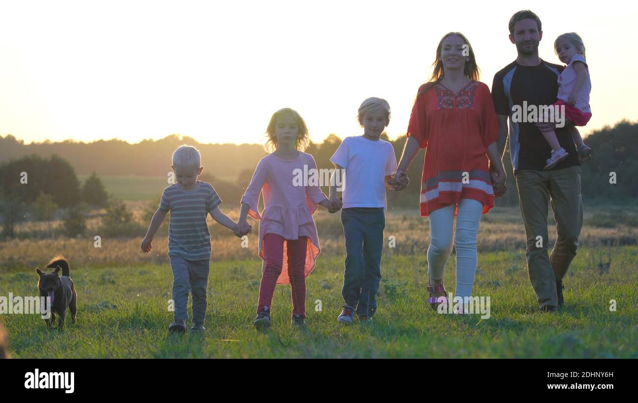 A large friendly family walks across the field at sunset with dog Stock ...