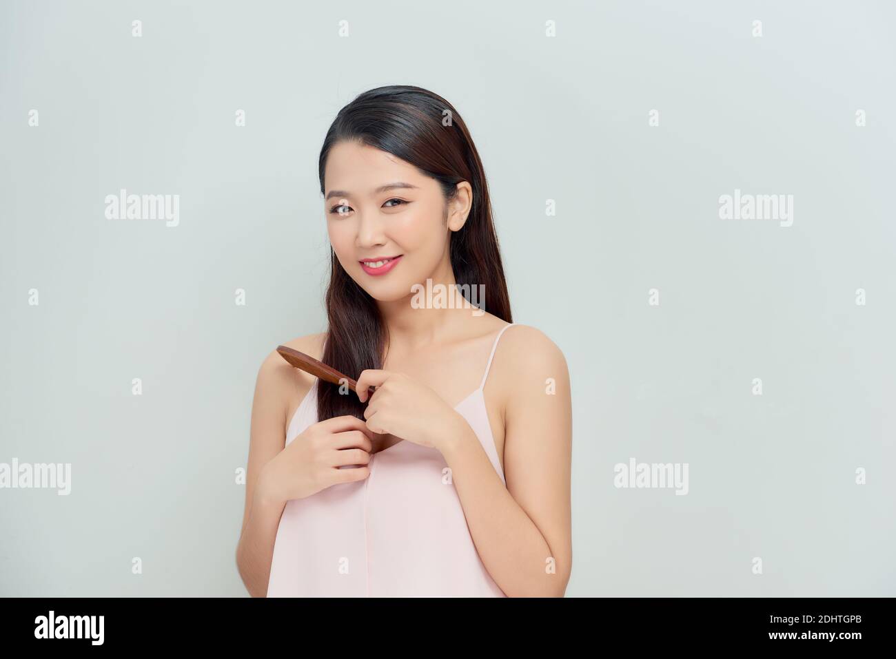 Portrait of cute young woman on white background combing hair. Stock Photo