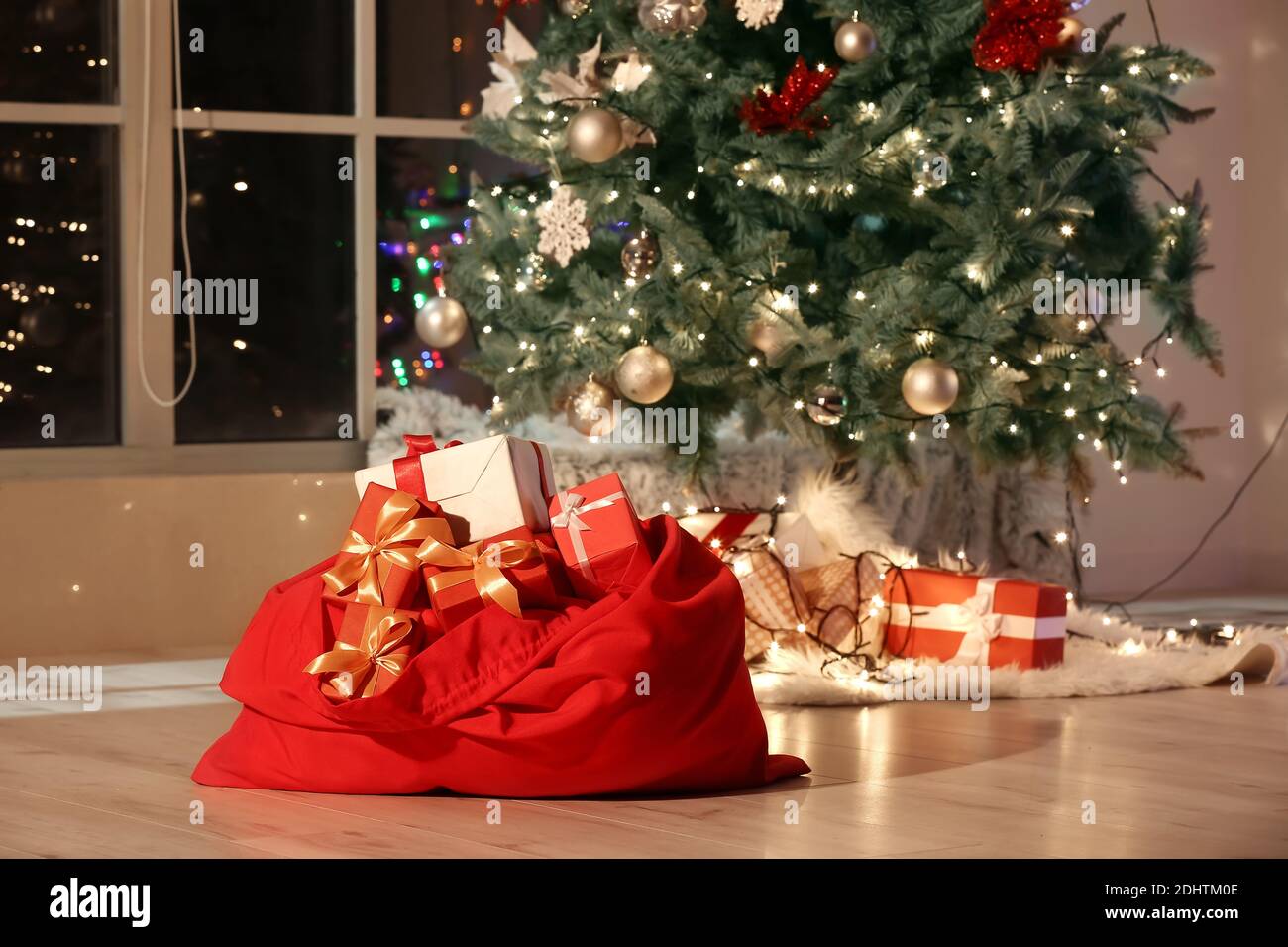 Santa bag with gifts and beautiful Christmas tree in room at night ...