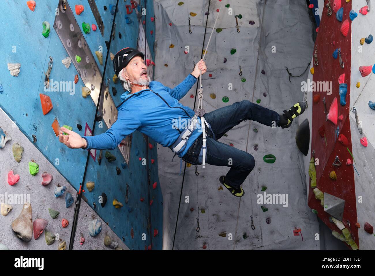 Professional senior man flying after jump while he is climbing on an artificial rock climbing wall. Extreme sports concept. Stock Photo