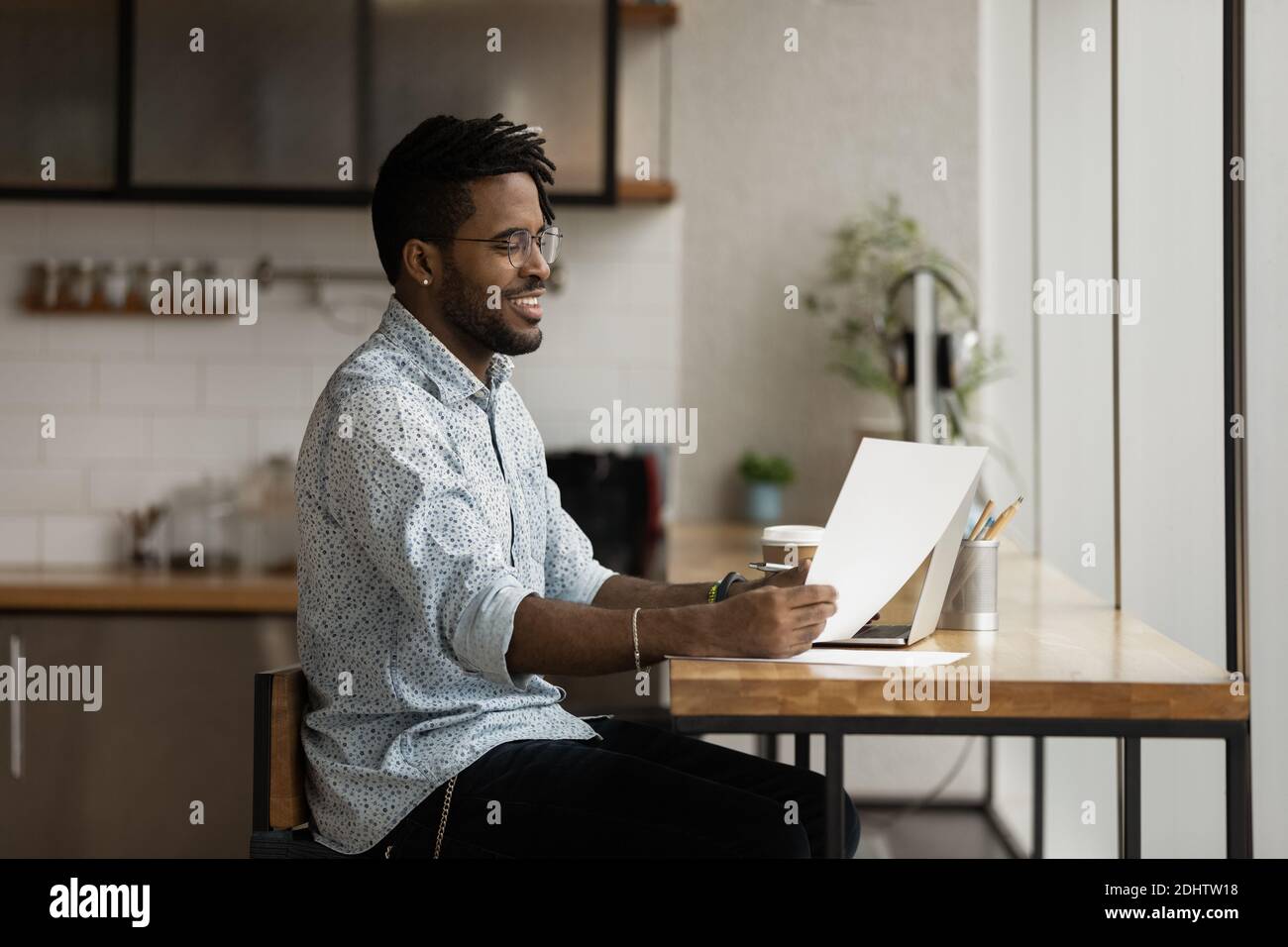 Smiling biracial man work on laptop reading paper document Stock Photo