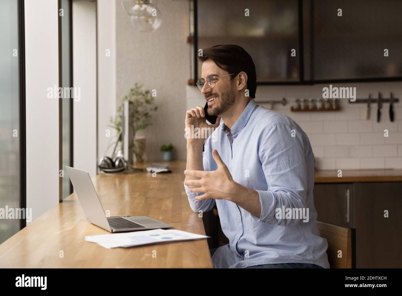 Smiling man work on laptop talking on smartphone Stock Photo