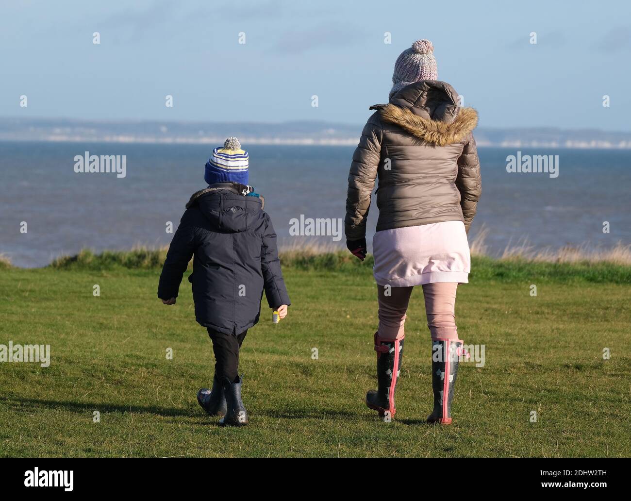 Woman and child walking on coastal cliff top in cool autumn weather. Stock Photo