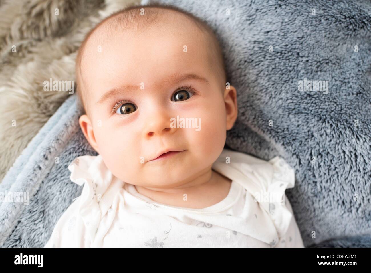 Portrait of baby with big eyes, lie on back and looks up at camera. Stock Photo