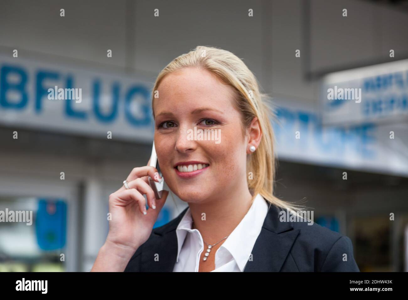 Eine Geschäftsfrau telefoniert mit ihrem Handy am Flughafen. Roaminggebühren bei Smartphones im Ausland, MR:YES Stock Photo